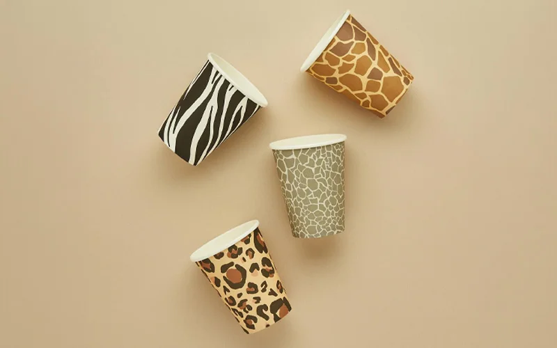 A collection of safari-themed paper cups displayed against a neutral beige background, featuring matching animal-inspired designs including zebra stripes, leopard print, giraffe markings and a grey textured pattern. The cups are arranged to highlight the coordinated safari party tableware collection. A collection of safari-themed paper cups displayed against a neutral beige background, featuring matching animal-inspired designs including zebra stripes, leopard print, giraffe markings and a grey textured pattern. The cups are arranged to highlight the coordinated safari party tableware collection.