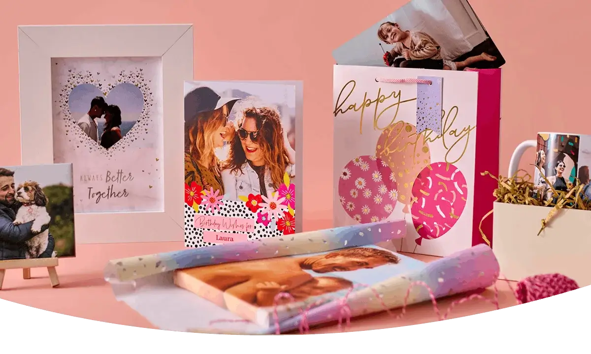Personalised gift collection featuring photo prints, a framed keepsake, a birthday gift bag, custom mugs, and personalised wrapping paper on a pink background.