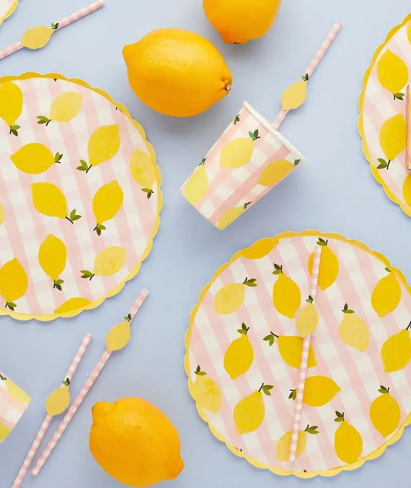 Lemon-themed party tableware with striped plates, cups, straws, and fresh lemons arranged on a light blue background Lemon-themed party tableware with striped plates, cups, straws, and fresh lemons arranged on a light blue background
