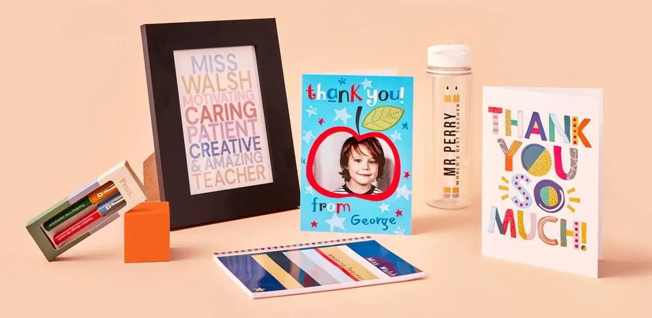 'A collection of teacher appreciation gifts including a teddy bear holding a heart with the text 'Amazing Teacher', a colorful thank you card, a candle with the text 'Thank you for an amazing Mrs. Khan', two small candles labeled 'Relax' and 'Calm', and a framed print with words describing Mrs. Khan such as motivating, caring, patient, creative, and amazing.'