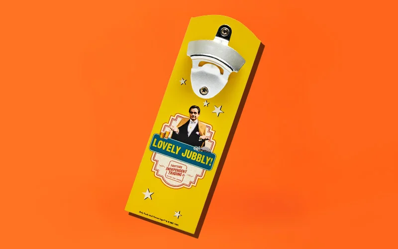 A yellow wall‑mounted bottle opener with a metal opener attached at the top, featuring a retro‑style label with the text ‘Lovely Jubbly’ and star details, displayed against a bright orange background. A yellow wall‑mounted bottle opener with a metal opener attached at the top, featuring a retro‑style label with the text ‘Lovely Jubbly’ and star details, displayed against a bright orange background.