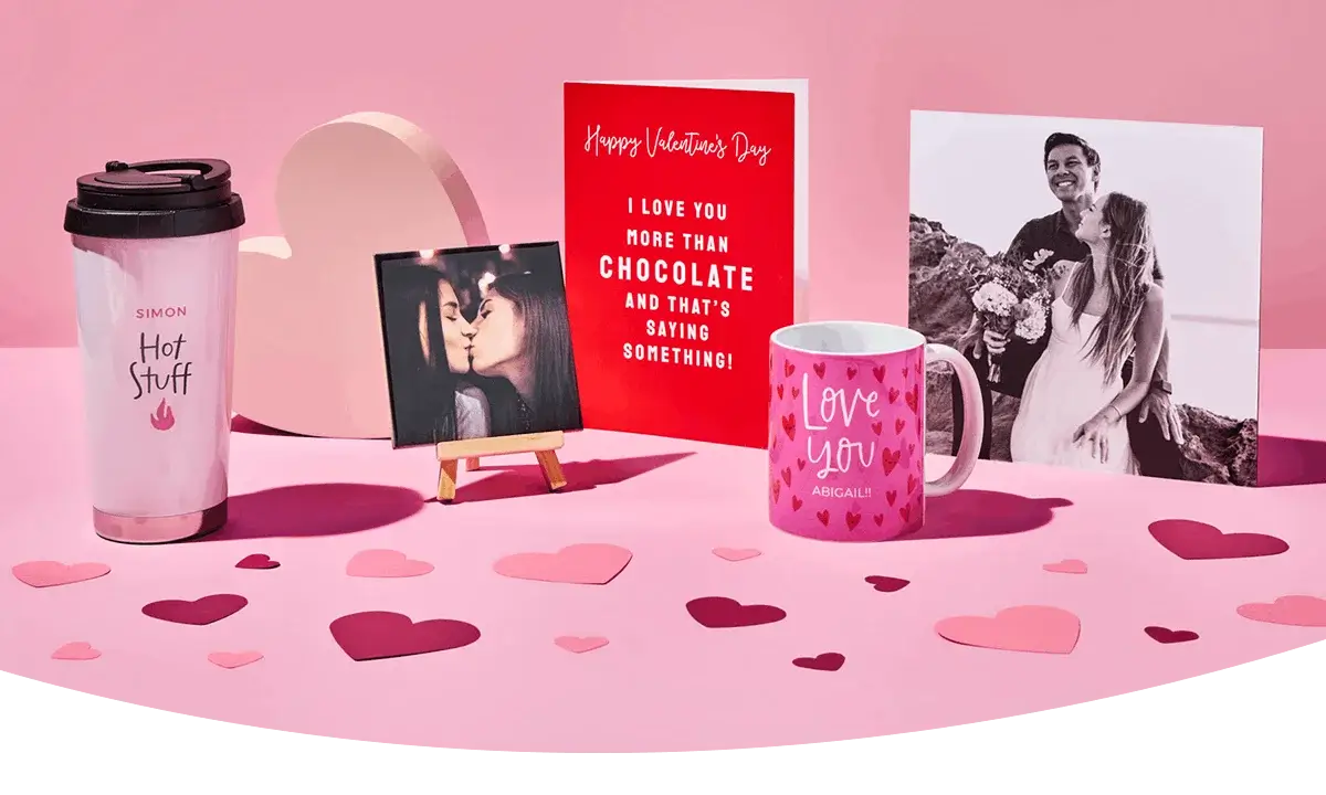 A Valentine’s display featuring a personalised travel cup, a framed photo, a bright red greeting card, a pink love‑themed mug, and a large romantic photo print, arranged on a pink surface with scattered heart cutouts. A Valentine’s display featuring a personalised travel cup, a framed photo, a bright red greeting card, a pink love‑themed mug, and a large romantic photo print, arranged on a pink surface with scattered heart cutouts.