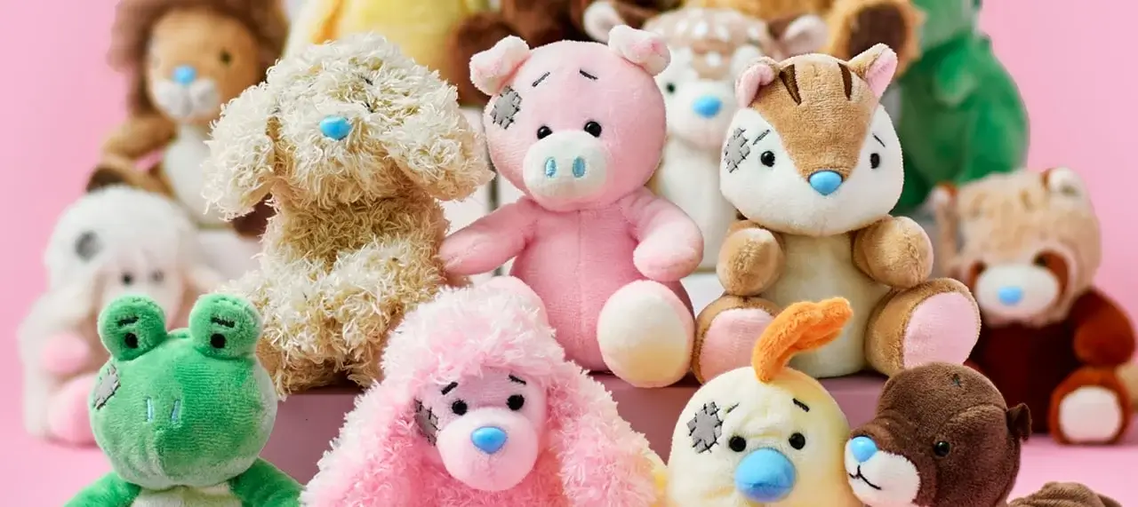 A group of stuffed animals arranged in rows on a pink background, including a lion, dog, pig, tiger, frog, and others, some with patchwork details.