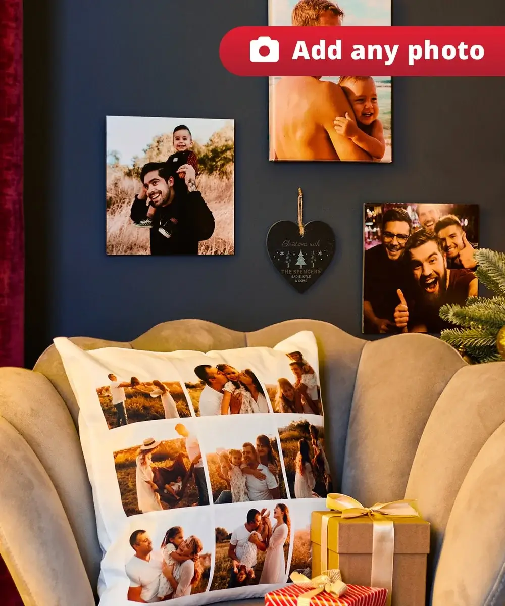 Cozy living room with a photo collage pillow on a beige armchair, framed family photos on a dark blue wall, heart-shaped Christmas ornament, and a partially visible decorated Christmas tree. Cozy living room with a photo collage pillow on a beige armchair, framed family photos on a dark blue wall, heart-shaped Christmas ornament, and a partially visible decorated Christmas tree.