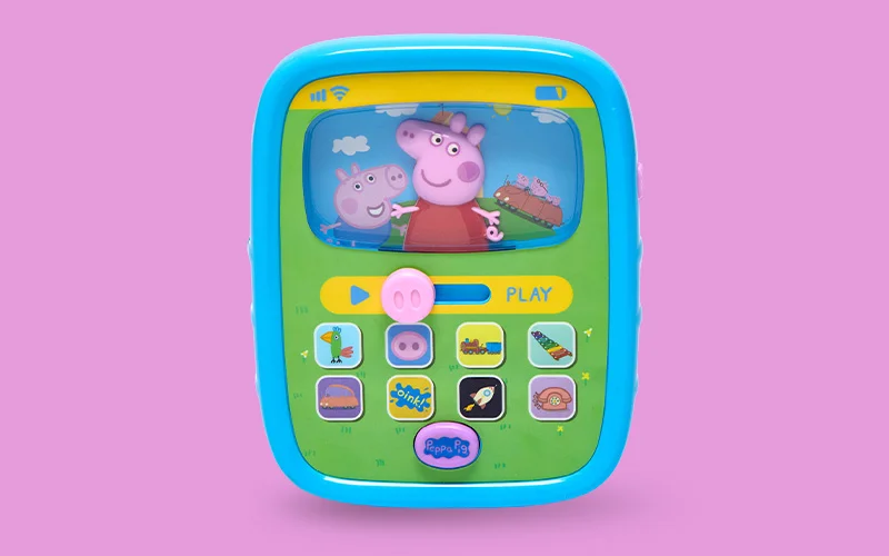 A Peppa Pig interactive children’s toy with a blue frame and green screen area, showing Peppa Pig on the display with colourful icon buttons below, against a pink background.