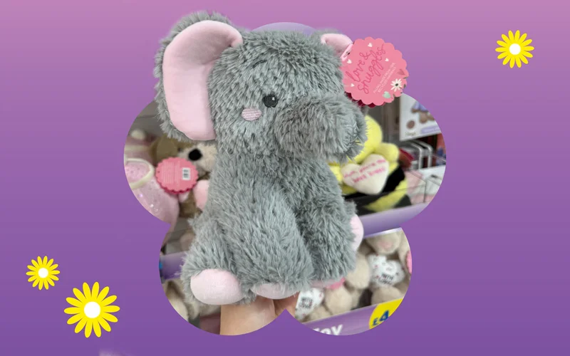 A fluffy grey elephant plush with pink inner ears and a decorative tag, shown against a purple and pink gradient background with small yellow daisy illustrations.