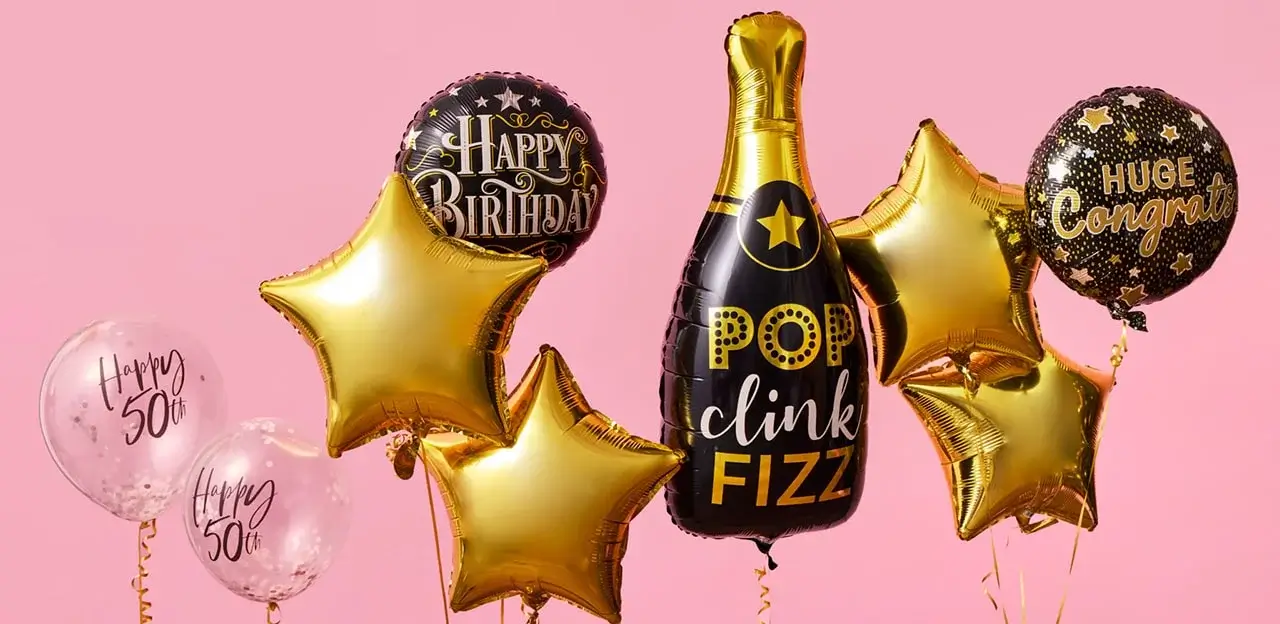 A group of celebratory balloons on a pink background, including gold stars, 'Happy 50th' balloons, and a champagne bottle-shaped balloon with the text 'POP clink FIZZ