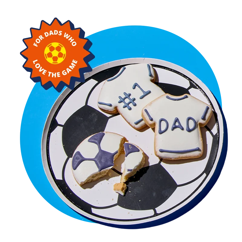 A football‑themed plate featuring black and white panel design, holding iced biscuits shaped like football shirts with ‘#1’ and ‘Dad’ written on them, along with a partially eaten football‑patterned biscuit, displayed against a bright blue background with a ‘For dads who love the game’ badge in the corner. A football‑themed plate featuring black and white panel design, holding iced biscuits shaped like football shirts with ‘#1’ and ‘Dad’ written on them, along with a partially eaten football‑patterned biscuit, displayed against a bright blue background with a ‘For dads who love the game’ badge in the corner.