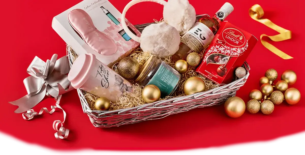Gift hamper on a red background containing earmuffs, a pink water bottle, a candle, Lindt chocolates, a small bottle of gin, and festive gold ornaments.