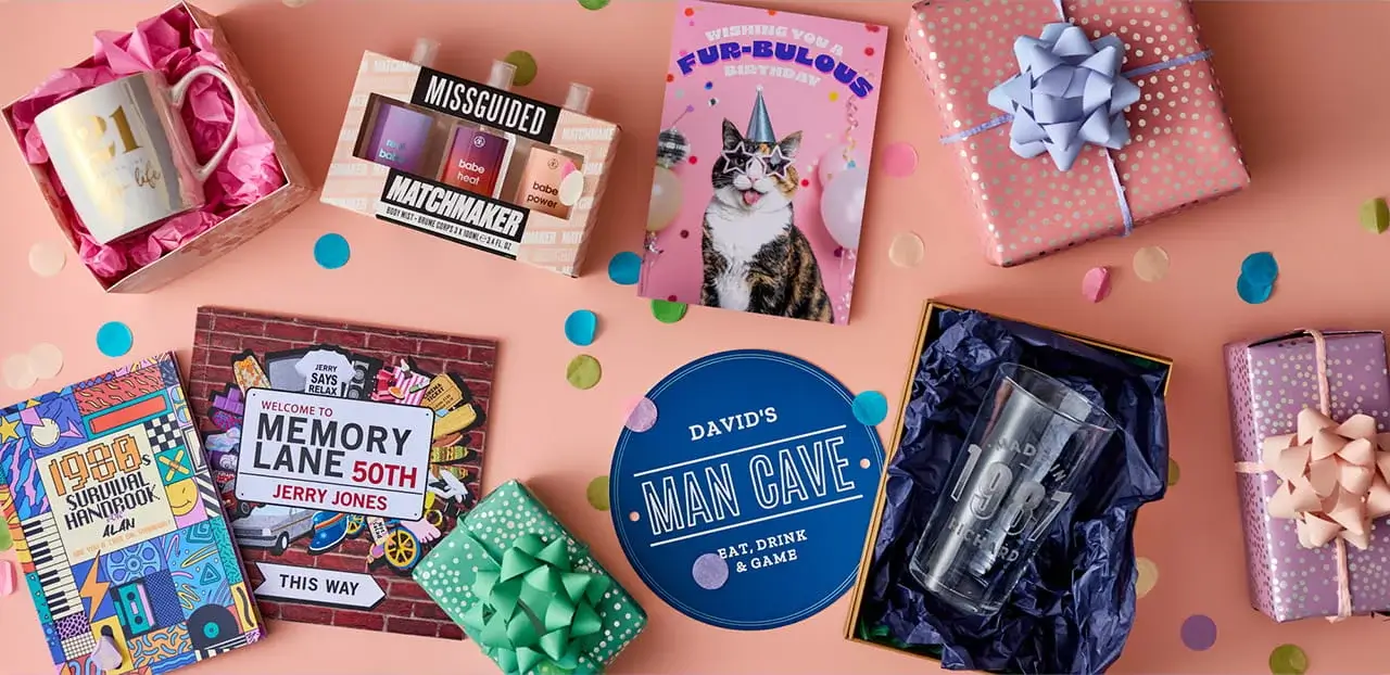Birthday gift collection featuring personalised mugs, glasses, books, gift sets, greeting cards, wrapped presents, and milestone birthday keepsakes on a pink background.