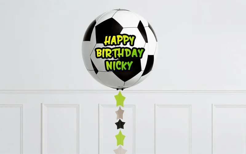 A round football-shaped foil balloon personalised with the message ‘Happy Birthday Nicky’ in green and yellow lettering, suspended above a hanging star garland against a white panelled background. A round football-shaped foil balloon personalised with the message ‘Happy Birthday Nicky’ in green and yellow lettering, suspended above a hanging star garland against a white panelled background.