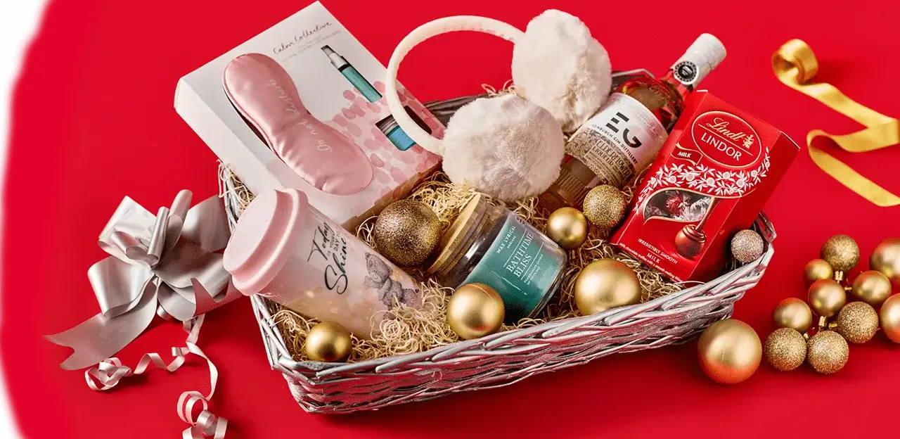 Gift hamper on a red background containing earmuffs, a pink water bottle, a candle, Lindt chocolates, a small bottle of gin, and festive gold ornaments. Gift hamper on a red background containing earmuffs, a pink water bottle, a candle, Lindt chocolates, a small bottle of gin, and festive gold ornaments.