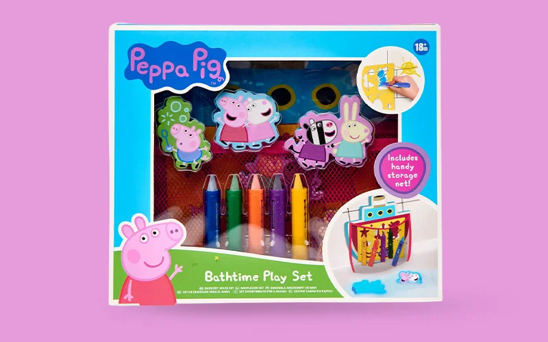 A boxed Peppa Pig bathtime play set displayed on a pink background, featuring colourful bath crayons, character water squirters, a storage net, and Peppa Pig graphics on the packaging.