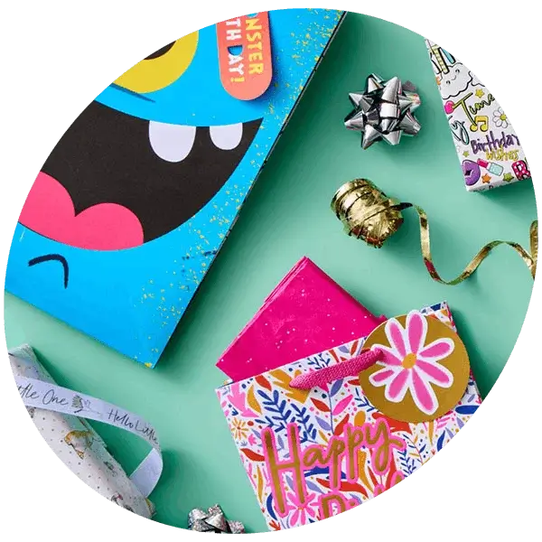 Colourful gift wrap set with birthday cards, patterned gift bags, ribbons, and bows arranged on a green background