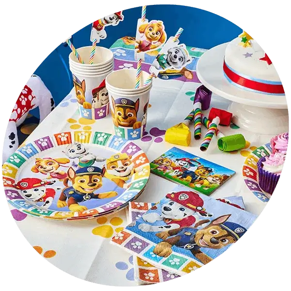 A colorful Paw Patrol-themed birthday party setup featuring a decorated cake with a number 9 candle, plates, cups, and napkins adorned with Paw Patrol characters. The table also includes party hats, gift bags, and various decorations such as a banner and hanging spirals.
