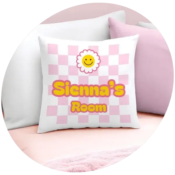 A white cushion with a pink checkered pattern and a smiling flower graphic, featuring the text Sienna’s Room.
