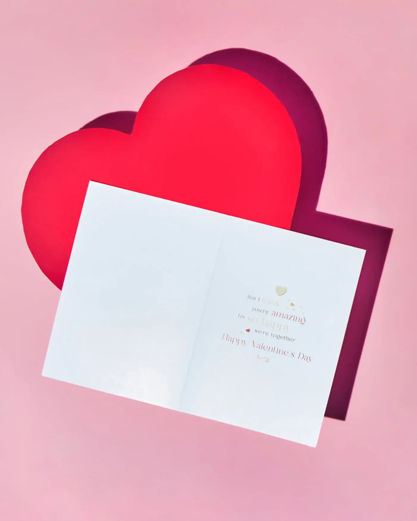 Open Valentine’s card displayed on a pink background with a large red heart shape behind it.