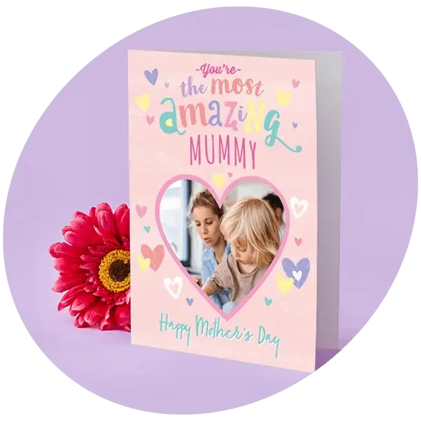 Pink Mother’s Day card decorated with colourful hearts and playful lettering, featuring a heart‑shaped photo window and displayed beside a bright pink flower on a pastel background.
