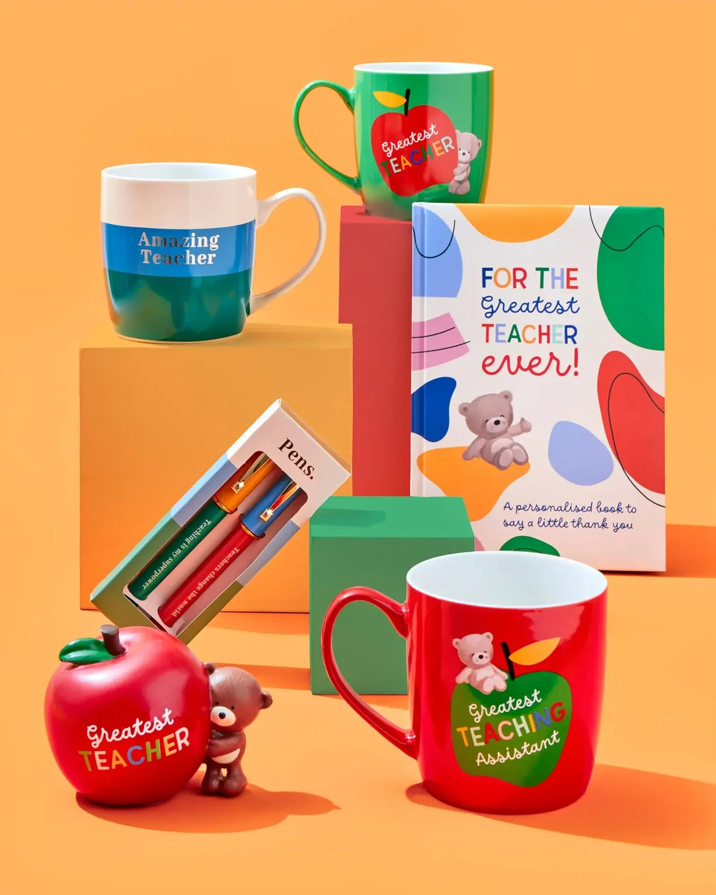 'A collection of teacher appreciation gifts including mugs, a personalized book, pens, and an apple-shaped container.' 'A collection of teacher appreciation gifts including mugs, a personalized book, pens, and an apple-shaped container.'