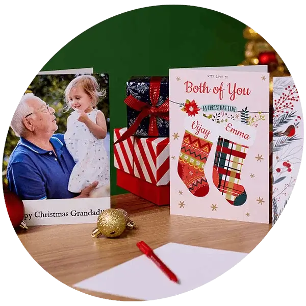 Personalised Christmas cards displayed with wrapped presents, festive decorations, and a family photo card on a wooden table.
