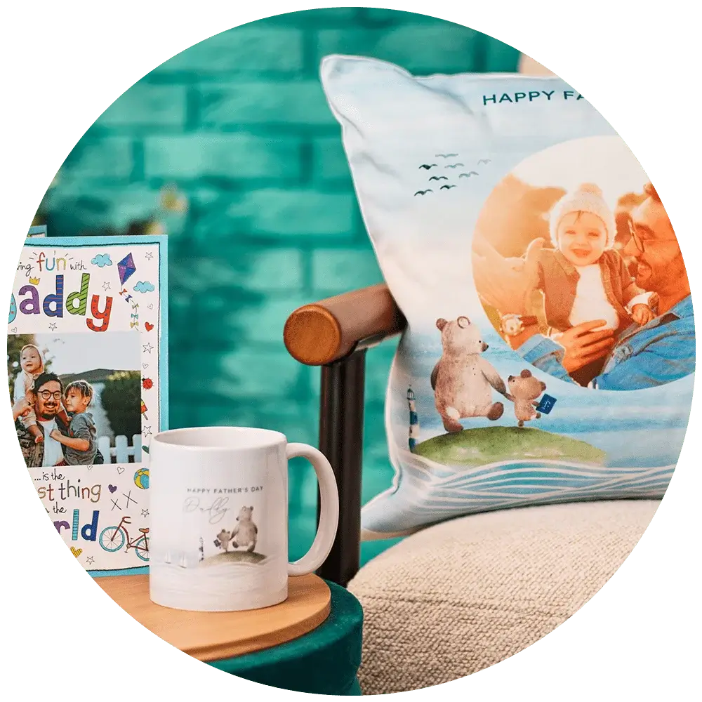 A Father's Day-themed setup featuring a greeting card, a mug, and a pillow. The greeting card has colorful text that reads 'Happy Father's Day' and 'Daddy' with playful illustrations. The white mug has an illustration of two bears and the text 'Happy Father's Day.' The pillow shows an illustration of a father bear reading to a child bear with the text 'HAPPY FATHER'S DAY' at the top.' A Father's Day-themed setup featuring a greeting card, a mug, and a pillow. The greeting card has colorful text that reads 'Happy Father's Day' and 'Daddy' with playful illustrations. The white mug has an illustration of two bears and the text 'Happy Father's Day.' The pillow shows an illustration of a father bear reading to a child bear with the text 'HAPPY FATHER'S DAY' at the top.'