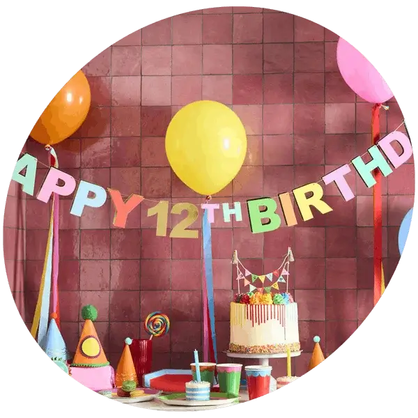 Colourful 12th birthday party setup with balloon banner, cake, party hats, and bright decorations on a tiled background