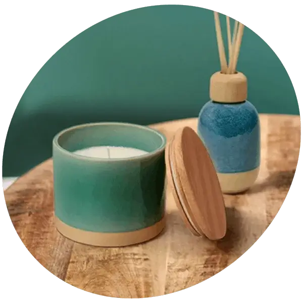 Ceramic candle and reed diffuser gift set displayed on a wooden surface against a teal background.