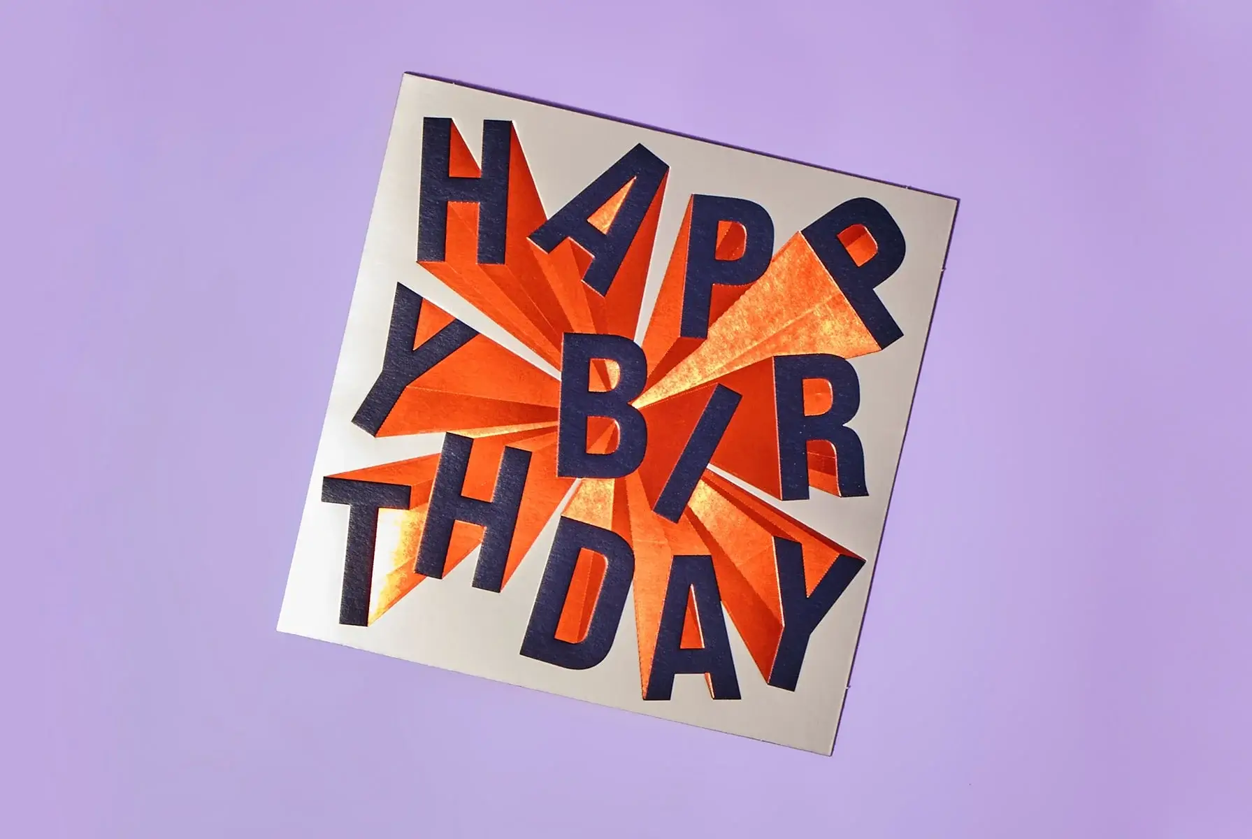 'A square greeting card with the words 'HAPPY BIRTHDAY' in bold, dark letters arranged in a scattered pattern over an orange starburst background. The card is set against a light purple backdrop.' 'A square greeting card with the words 'HAPPY BIRTHDAY' in bold, dark letters arranged in a scattered pattern over an orange starburst background. The card is set against a light purple backdrop.'
