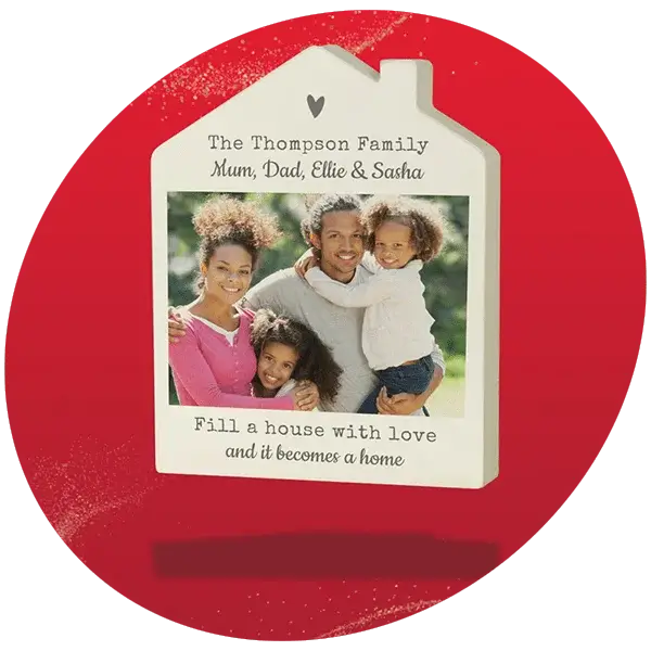House-shaped photo frame with personalized text reading “The Thompson Family Mum, Dad, Ellie & Sasha” and the phrase “Fill a house with love and it becomes a home,” displayed against a bright red background.