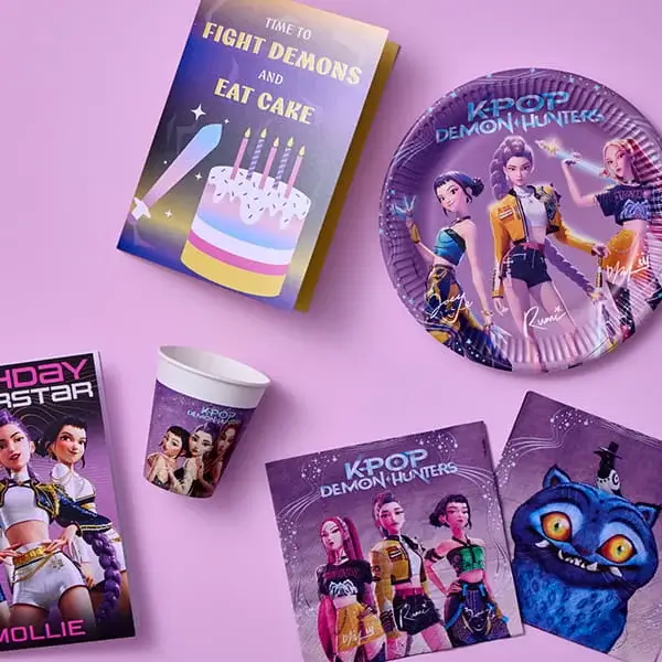 K-pop Demon Hunters themed party tableware with character plates, cups, napkins, and a birthday card on a pastel pink background