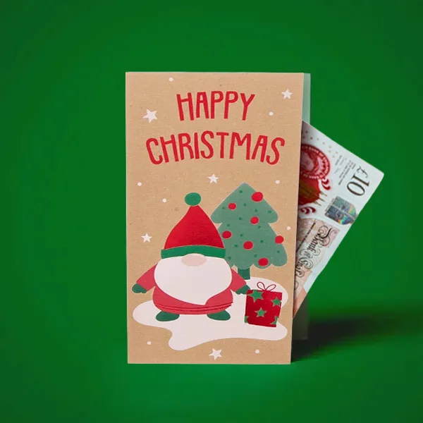 A Christmas-themed money wallet featuring a gnome illustration, a decorated Christmas tree and the text ‘Happy Christmas,’ displayed with a banknote partially visible inside against a green background.