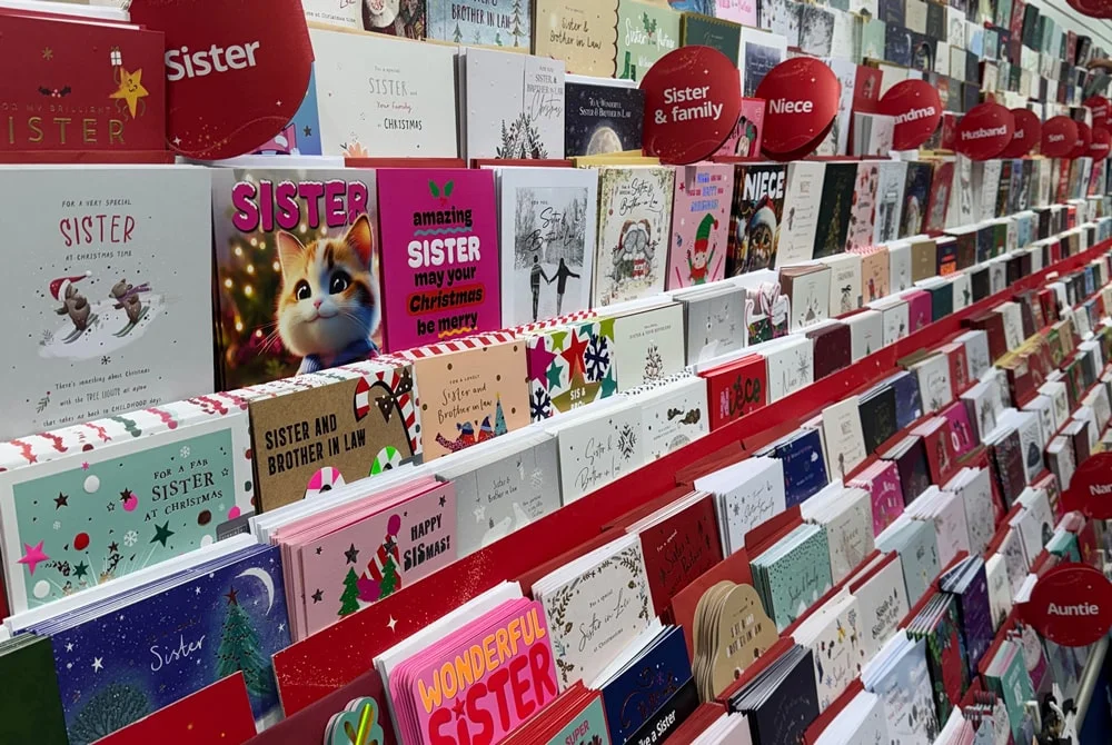 A store display filled with Christmas cards organized by recipient categories such as sister, niece, and grandma, featuring various festive designs and colors. A store display filled with Christmas cards organized by recipient categories such as sister, niece, and grandma, featuring various festive designs and colors.