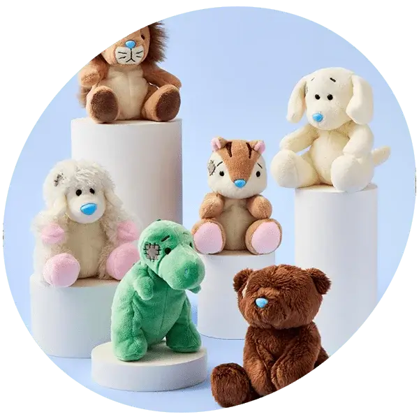 A group of six plush toys arranged on white cylindrical pedestals against a light blue background. The toys include a brown lion, a cream-colored dog, a white sheep with pink ears and feet, a green dinosaur with a stitched patch on its face, an orange and brown chipmunk with pink feet, and a brown bear.