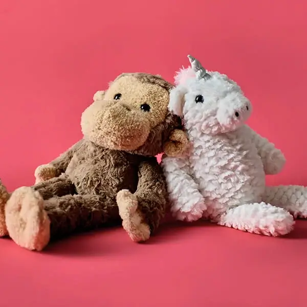 Two plush toys, a brown monkey and a white unicorn with a silver horn, sitting together against a bright pink background.