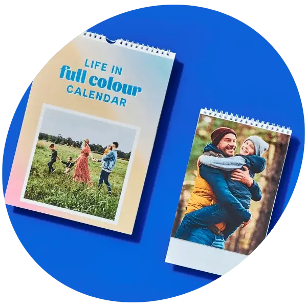 Two spiral-bound calendars on a blue background, one with a family walking in a field and the other showing two people embracing outdoors.