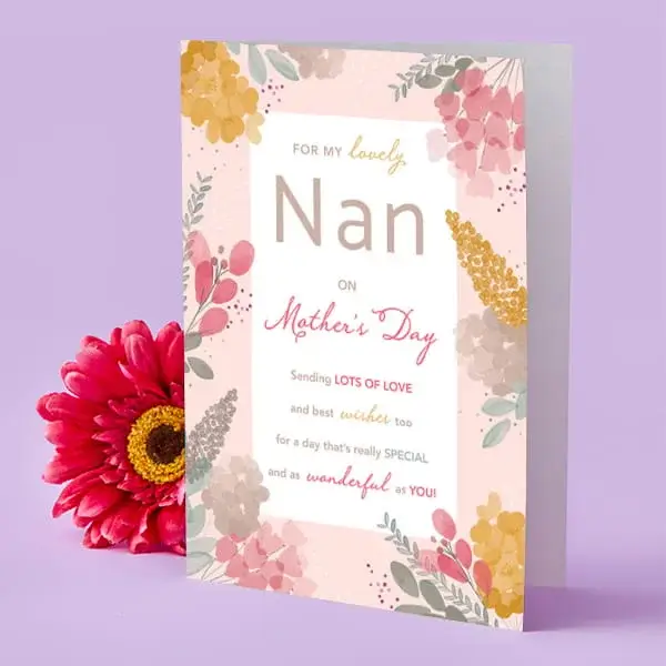 A pastel floral Mother’s Day card for a nan, decorated with soft pink, yellow, and gold-toned flowers, displayed upright beside a bright pink flower.