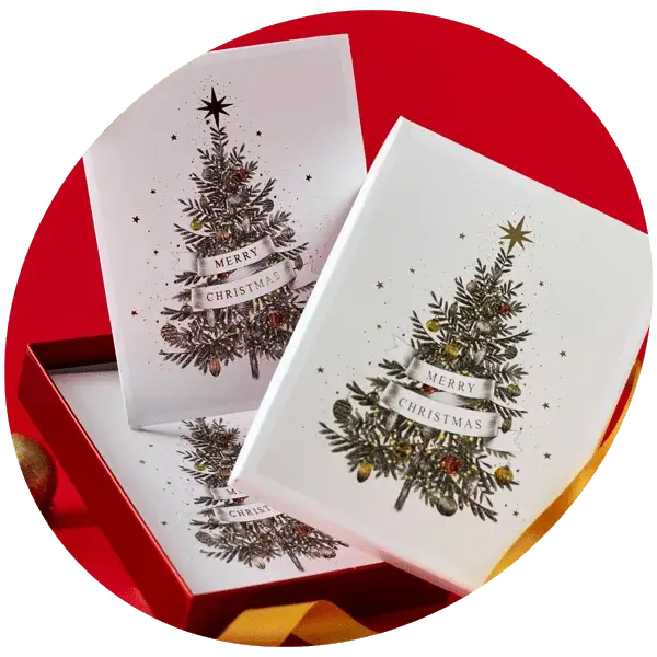 A set of three Christmas cards featuring a decorated Christmas tree with the text 'Merry Christmas' on a white background. The cards are placed in an open red box with a yellow ribbon, against a red backdrop.