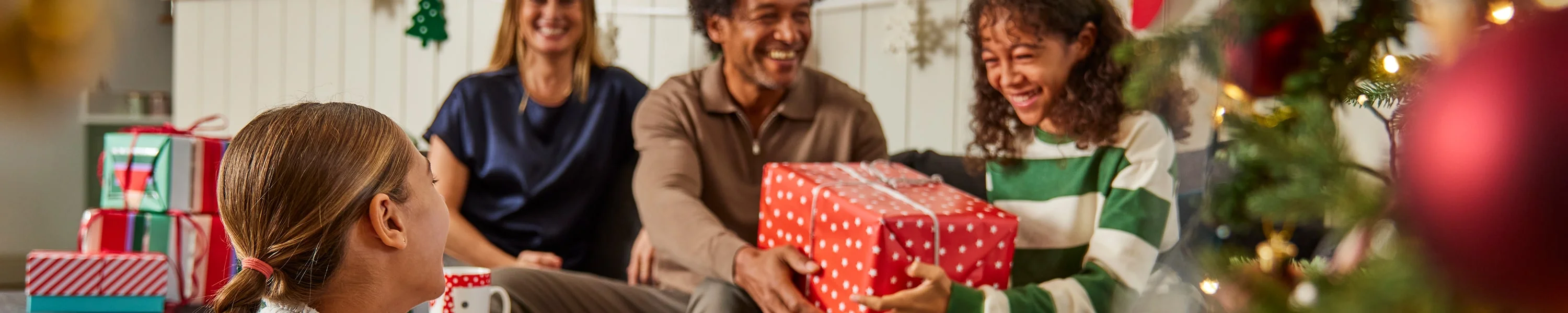 A festive living room scene with people exchanging wrapped gifts near a decorated Christmas tree. A festive living room scene with people exchanging wrapped gifts near a decorated Christmas tree.