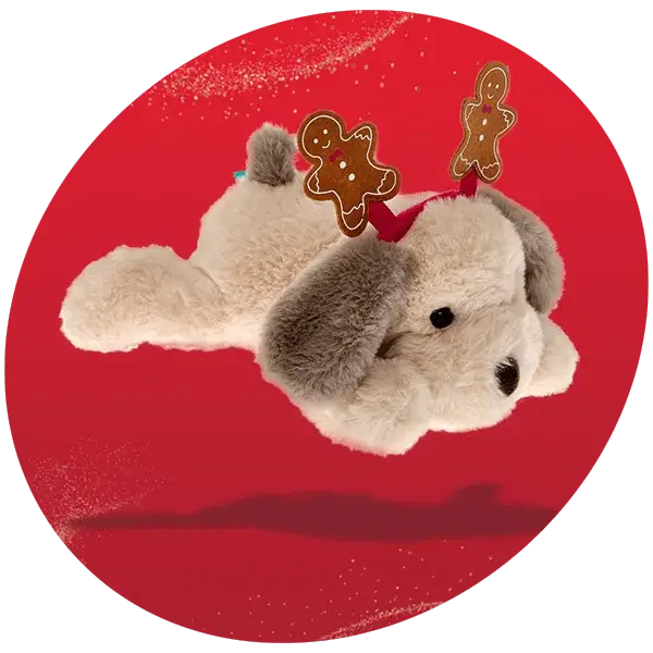 Plush dog toy with floppy gray ears wearing a festive headband decorated with two gingerbread men, displayed against a bright red background.