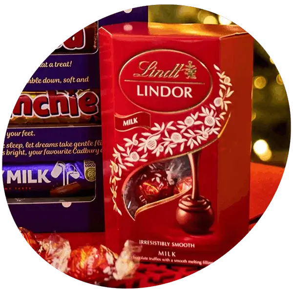 Box of Lindt Lindor milk chocolates alongside assorted chocolate treats on a festive background