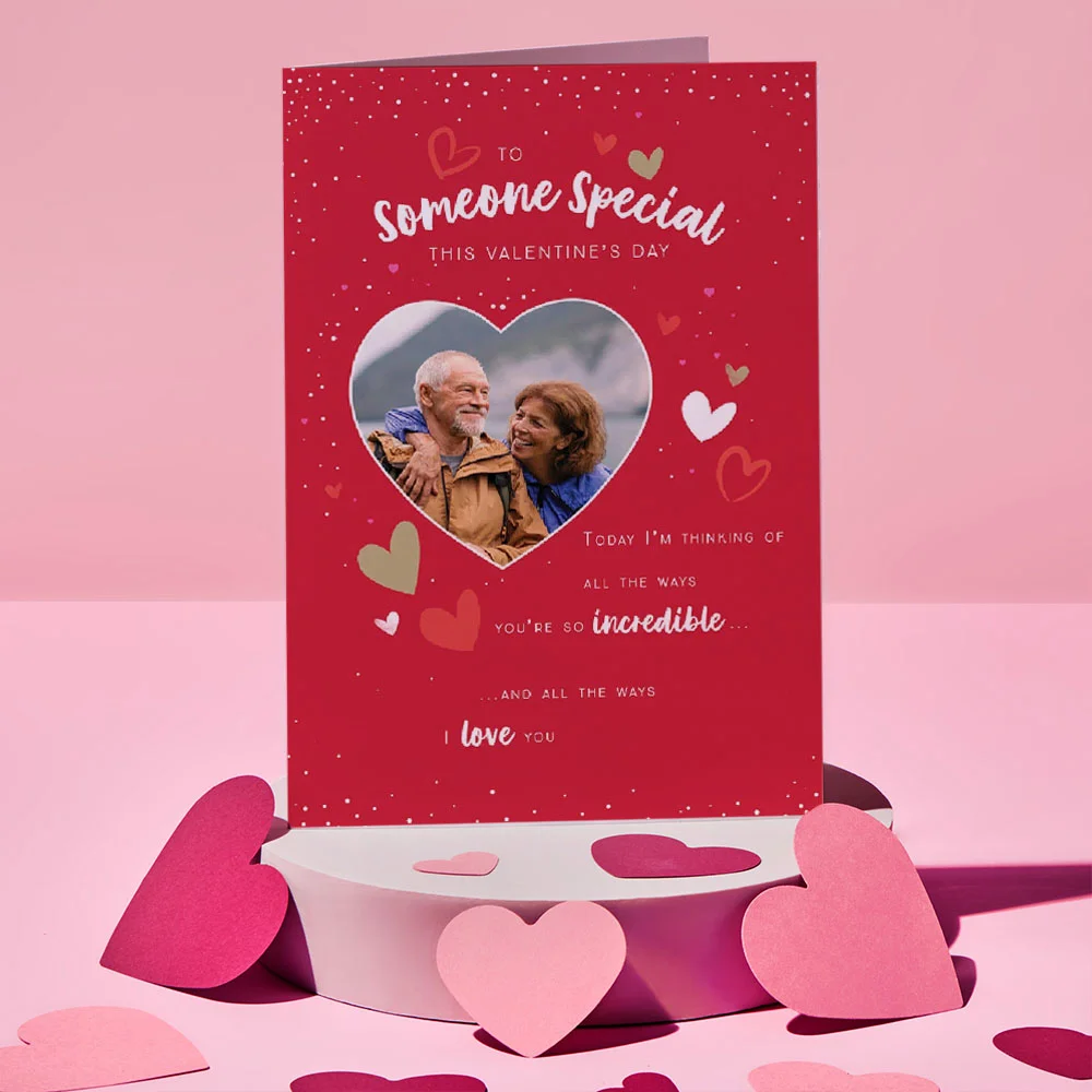 Green plush frog with a gold crown holding a red heart that says Kiss Me, set against a pink background with a large heart shape.