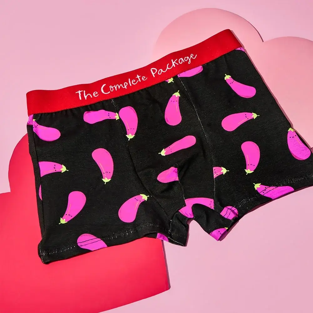 Red and gold artificial rose displayed under a clear glass dome on a round base, surrounded by pink and red paper hearts on a pink background.