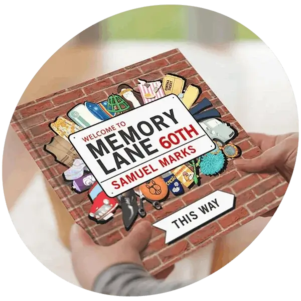 A personalised memory lane print held in hands, designed like a brick wall street sign with illustrated icons and text welcoming someone to Memory Lane with a 60th birthday and name detail.