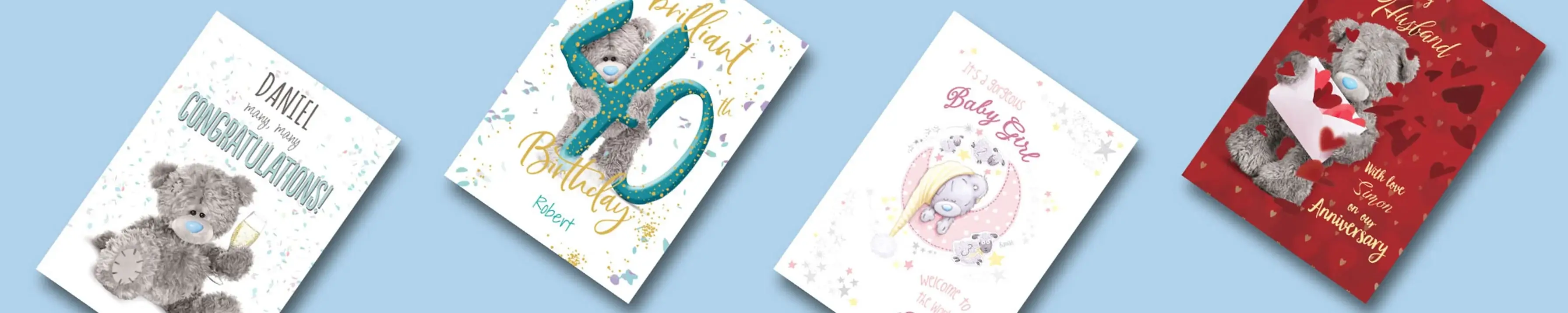 The image shows four greeting cards on a light blue background. The first card on the left is white with a grey teddy bear holding a champagne glass, and the text reads 'DANIEL many happy CONGRATULATIONS!'. The second card is also white with a grey teddy bear holding large turquoise numbers '40', and the text reads 'Brilliant 40th Birthday Robert'. The third card is white with a grey teddy bear wearing a yellow hat, surrounded by stars, and the text reads 'It's A Precious Baby Girl Welcome To The World'. The fourth card is red with hearts in the background, featuring a grey teddy bear holding an envelope with hearts coming out of it, and the text reads 'To My Husband with love from me on our Anniversary