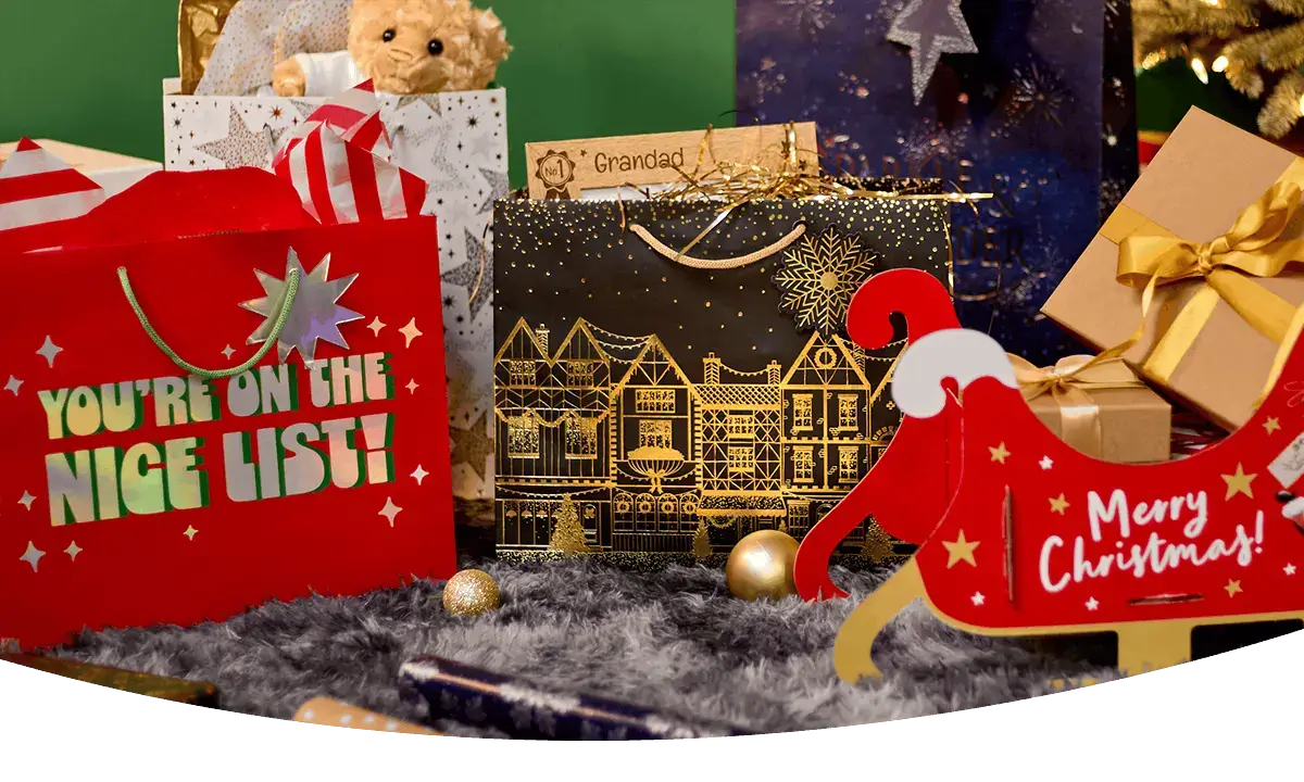 Christmas gift bags, wrapped presents and a festive Santa sleigh gift set displayed in front of a decorated Christmas tree.