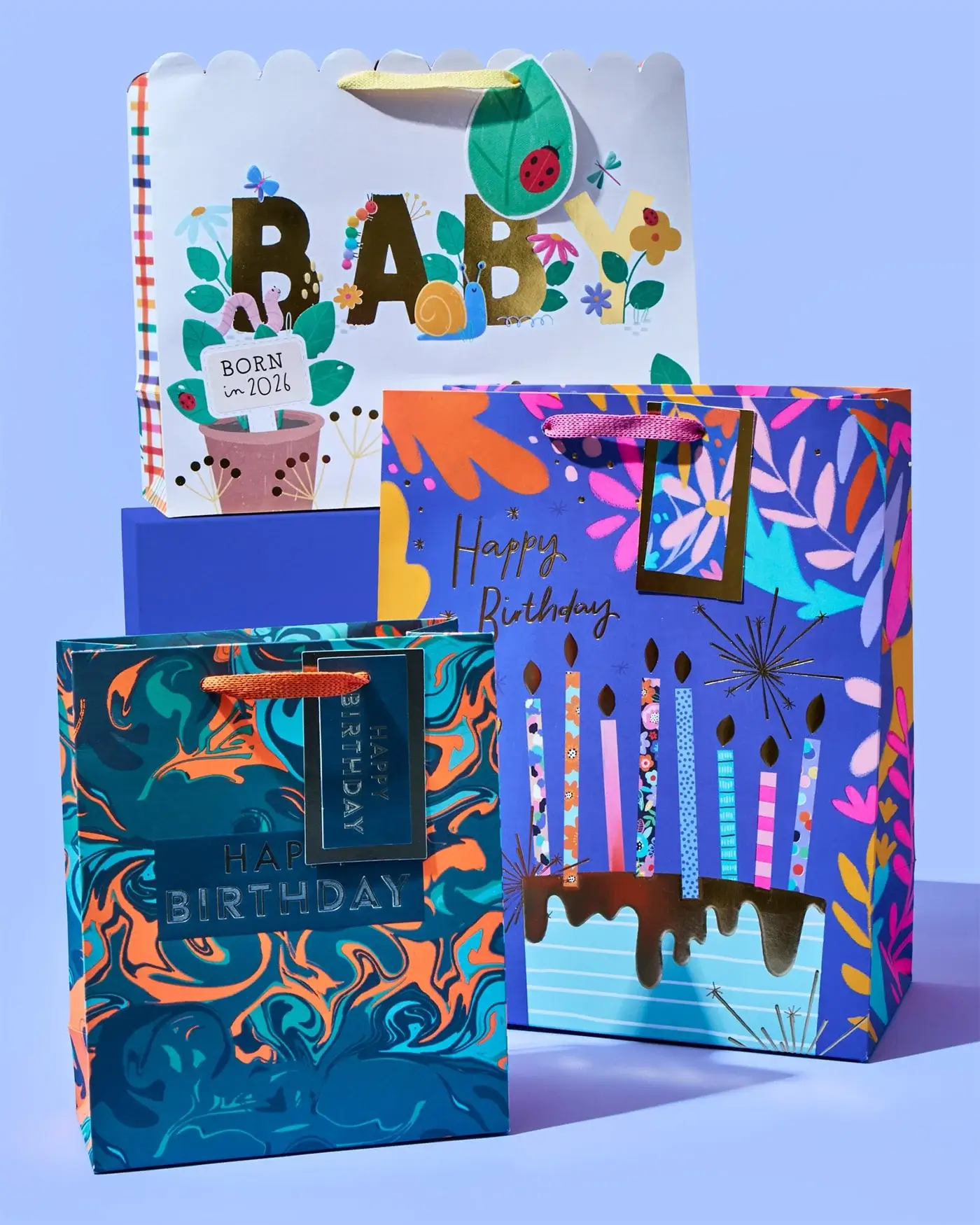 'The image shows three colorful gift bags with different designs. The first bag has the word BABY in large letters and a tag that reads BORN IN 2021. The second bag has a vibrant floral design with the words Happy Birthday and candles on it. The third bag features a blue and orange marbled pattern with the words Happy Birthday embossed on it.' 'The image shows three colorful gift bags with different designs. The first bag has the word BABY in large letters and a tag that reads BORN IN 2021. The second bag has a vibrant floral design with the words Happy Birthday and candles on it. The third bag features a blue and orange marbled pattern with the words Happy Birthday embossed on it.'