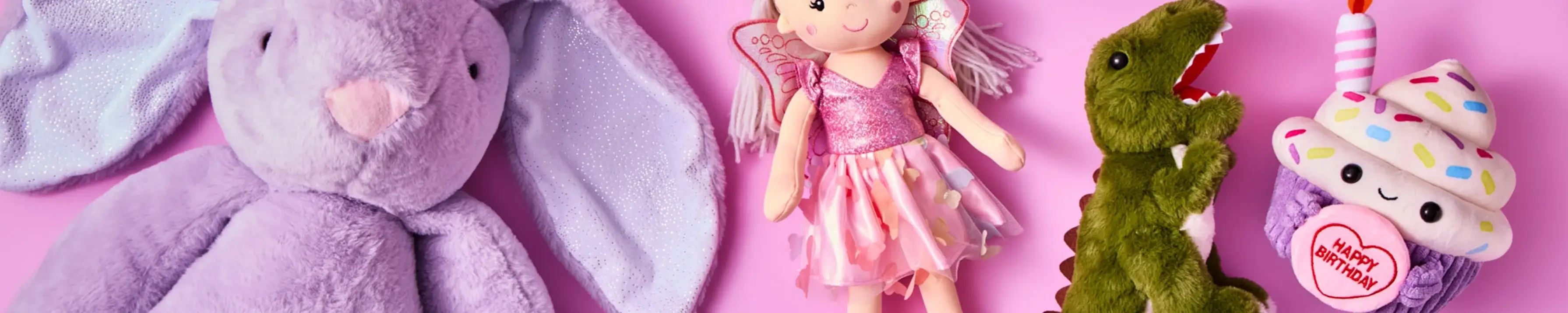 Four plush toys on a pink background: a purple bunny, a fairy doll in a pink dress, a green dinosaur, and a cupcake holding a Happy Birthday sign. Four plush toys on a pink background: a purple bunny, a fairy doll in a pink dress, a green dinosaur, and a cupcake holding a Happy Birthday sign.