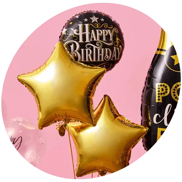 An open cardboard box filled with tissue paper and a small gift box, surrounded by colorful balloons. The central balloon is black with gold stars and the text 'HUGE Congrats!'