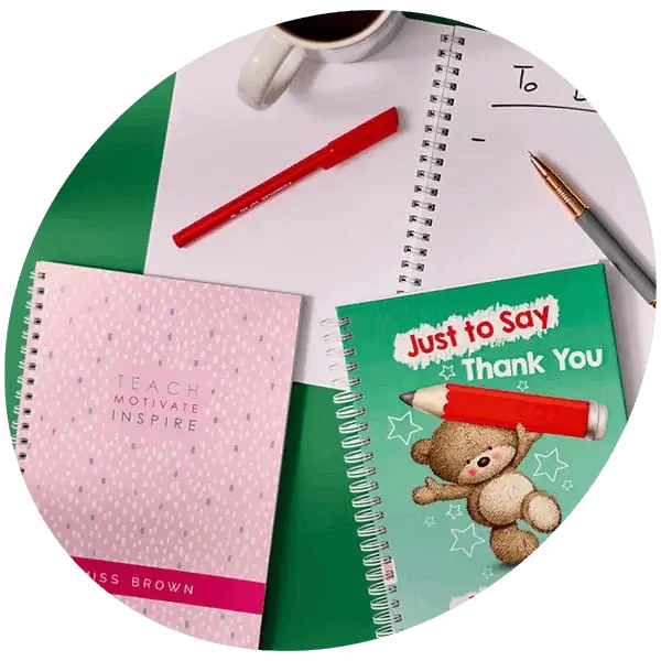 Teacher gift notebooks with personalised covers, pens, coffee mug, and a to do list arranged on a green background