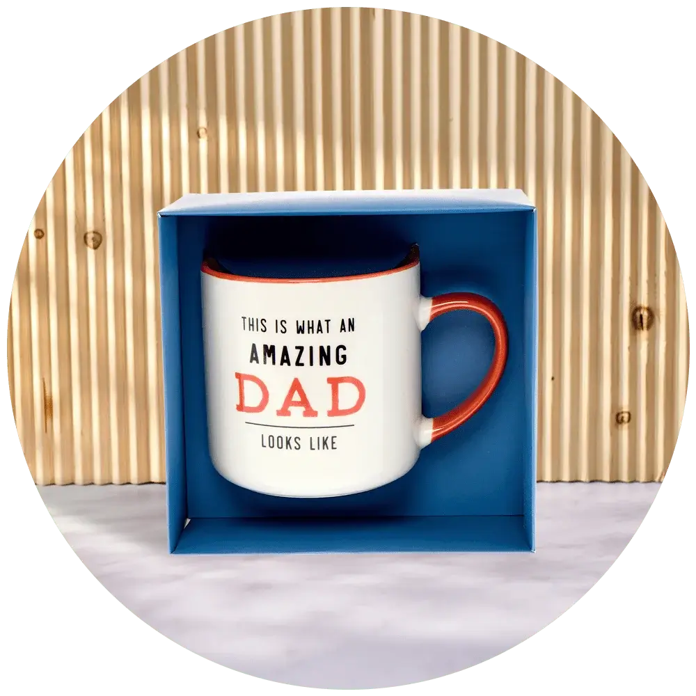 A white ceramic mug with a red handle and rim, displayed in a blue box. The mug has the text 'THIS IS WHAT AN AMAZING DAD LOOKS LIKE' printed on it, with the word 'DAD' in large red letters.' A white ceramic mug with a red handle and rim, displayed in a blue box. The mug has the text 'THIS IS WHAT AN AMAZING DAD LOOKS LIKE' printed on it, with the word 'DAD' in large red letters.'